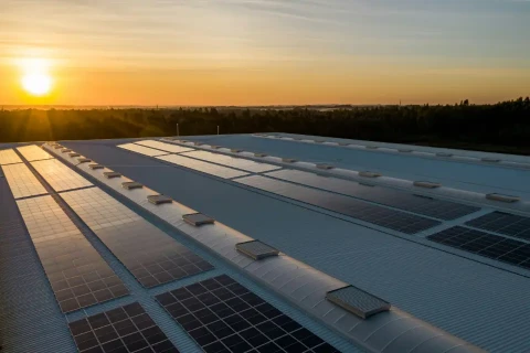 Schwarze Solarpanele auf einem großen flachen Gebäudedach mit Sonnenaufgang im Hintergrund.